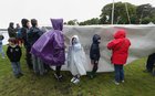 Peole cover up as the rain comes down before the launching of the paper boat in Kinvara.